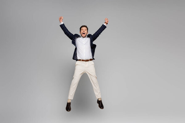 full length of excited man with outstretched hands jumping on grey