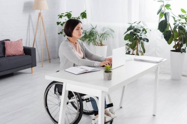 Masadaki kağıt ve defterin yanında çalışırken dizüstü bilgisayar kullanan engelli kadın 