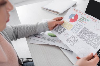 Paper with graphs in hands of freelancer on blurred foreground at home  clipart