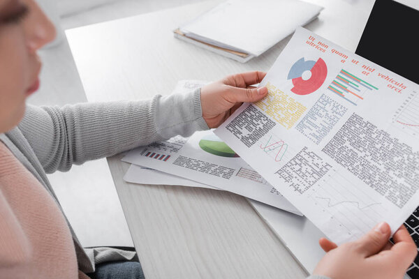 Paper with graphs in hands of freelancer on blurred foreground at home 