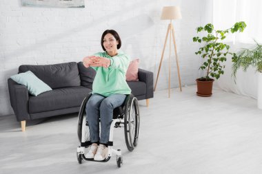 Evde antrenman yaparken tekerlekli sandalyede esneme hareketleri yapan pozitif bir kadın. 