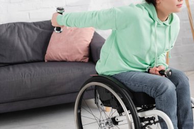 Engelli bir kadının evdeki kanepenin yanında dambıllarla çalışması. 