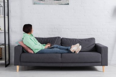 Oturma odasındaki kanepede dizüstü bilgisayar kullanan serbest çalışan 