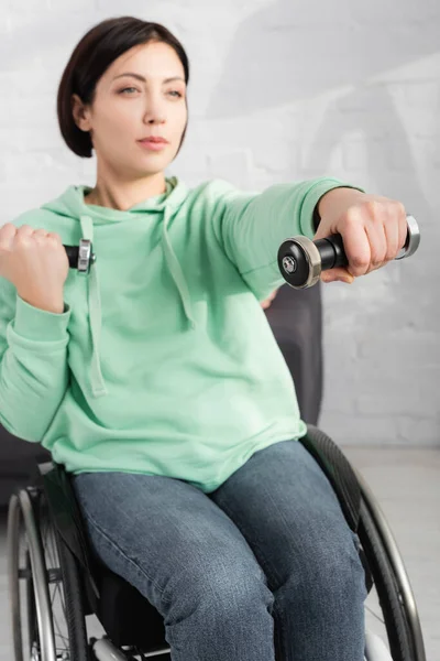 Dumbbell in hand of woman in wheelchair training on blurred background