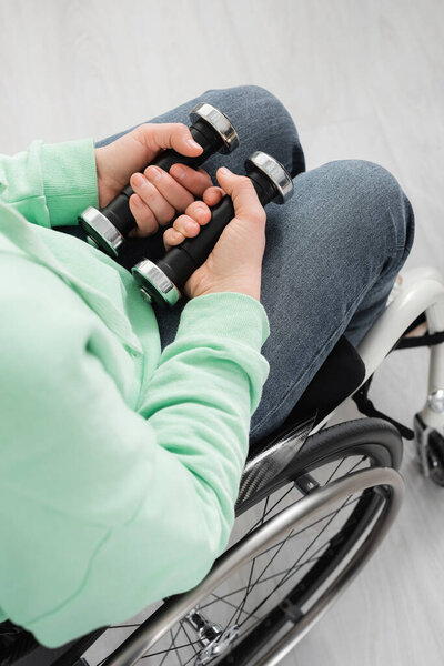 Вид сверху на женщину, держащую гантели в инвалидной коляске 