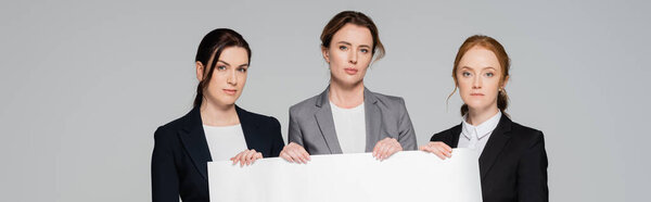 Businesswomen in formal wear holding white placard isolated on grey, banner 