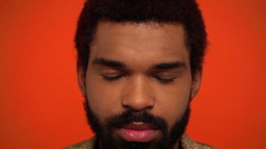 Afro-Amerikan adam somurtuyor ve kızgın turuncu üzerine izole ediliyor.