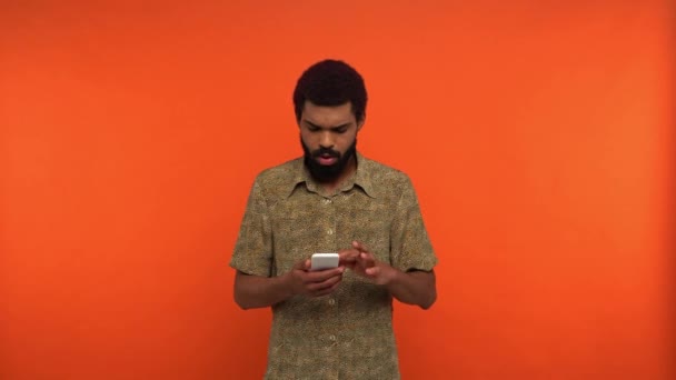 興奮したアフリカ系アメリカ人男性がオレンジに孤立したスマートフォンで — ストック動画