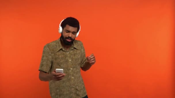 Afrikansk Amerikansk Man Trådlösa Hörlurar Med Smartphone Isolerad Orange — Stockvideo