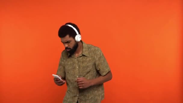 Afrikaans Amerikaanse Man Hoofdtelefoon Met Behulp Van Smartphone Geïsoleerd Oranje — Stockvideo