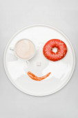 pohled na usmívající se obličej z latté v šálku, koblihy, kostky cukru a marmelády na kulatém podnosu na bílém