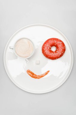 top view of smiling face made of latte in cup, doughnut, sugar cube and jam on round tray on white clipart