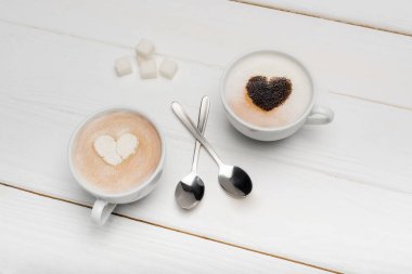 Beyaz ahşap yüzeyde kapuçino ve kaşık ve şeker küplerinin yanında latte ile bardakların üst görüntüsü 