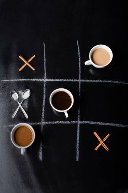 Kaşık, tarçın çubuğu ve siyah kahve fincanlarıyla yapılan tic tac toe oyununun en üst görüntüsü