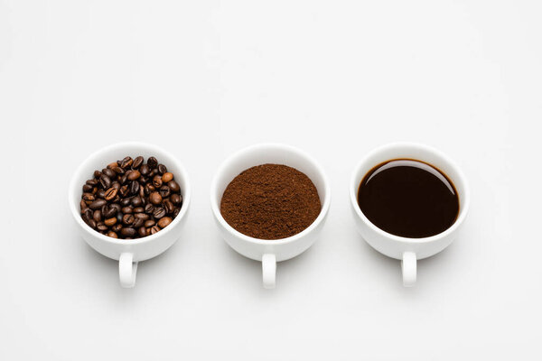 cups with prepared and ground coffee near beans on white