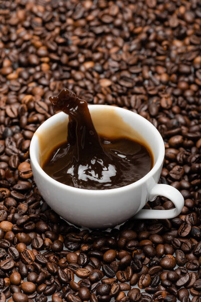 white cup with prepared coffee splashing on brown beans 