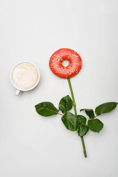 верхний вид чашки с латте возле пончика и зеленые листья имитирующие цветок на белом