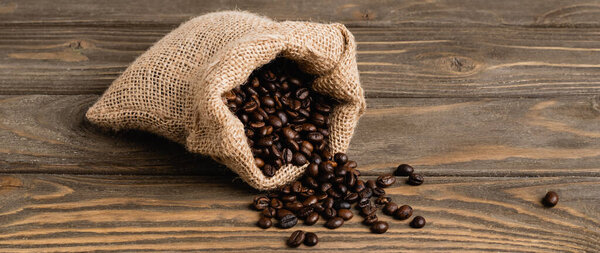sack bag with roasted coffee beans on wooden surface, banner