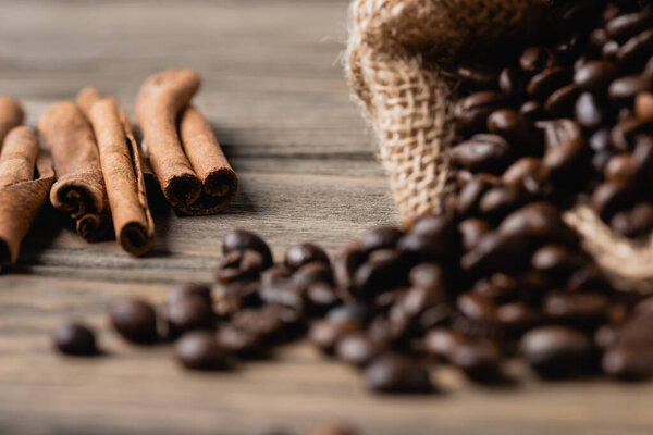 cinnamon sticks near sack bag with roasted coffee beans on blurred wooden surface 