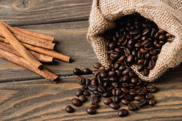 cinnamon sticks near sack bag with roasted coffee beans on wooden surface 