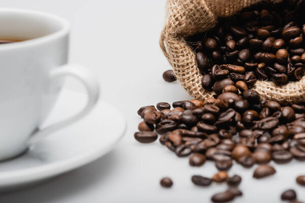 sack bag with roasted coffee beans near cup on blurred foreground 