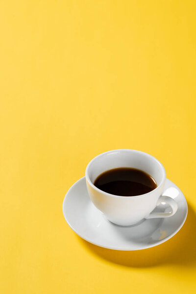 black coffee in white cup on yellow background 