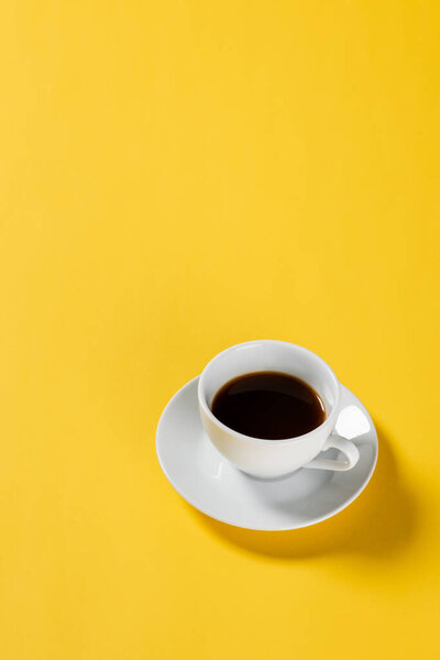 high angle view of black coffee in white cup on yellow background 