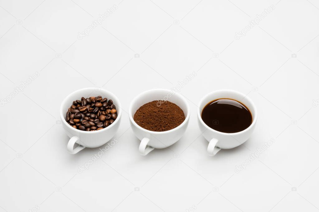 cups with ground and prepared coffee near beans on white