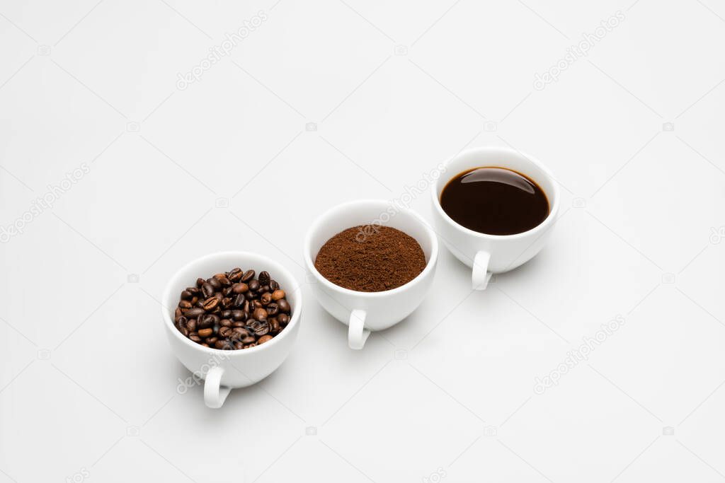 mugs with prepared and ground coffee near beans on white