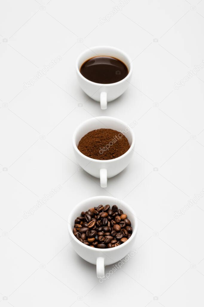 cups with beans, prepared and ground coffee on white