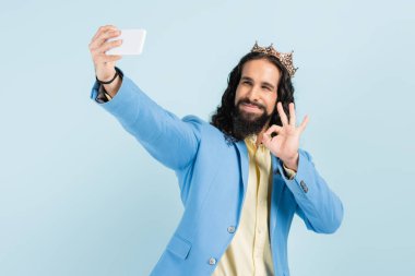 Mutlu İspanyol ceketli ve taclı adam iyi görünüyor ve mavi üzerinde selfie çekiyor.