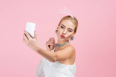 Sarışın kadın çubukta kağıt taç tutuyor ve pembe üzerine hava öpücüğü gönderirken selfie çekiyor.