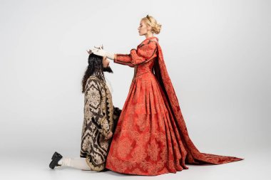 Orta çağ giysili İspanyol kralın tacını takan sarışın kraliçe dizlerinin üzerinde duruyor.