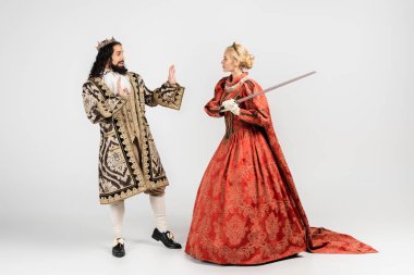 Orta çağ kıyafetleri içindeki korkak İspanyol kralın yanında elinde kılıç tutan sarışın bir kraliçe.