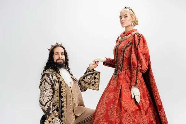 hispanic king in crown and medieval clothing holding hand of blonde queen on white