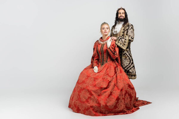 interracial king and queen in medieval clothing and crowns looking at camera on white