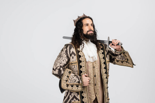 латиноамериканский король в средневековой одежде и короне, держащий меч, глядя вдали, изолированный на белом