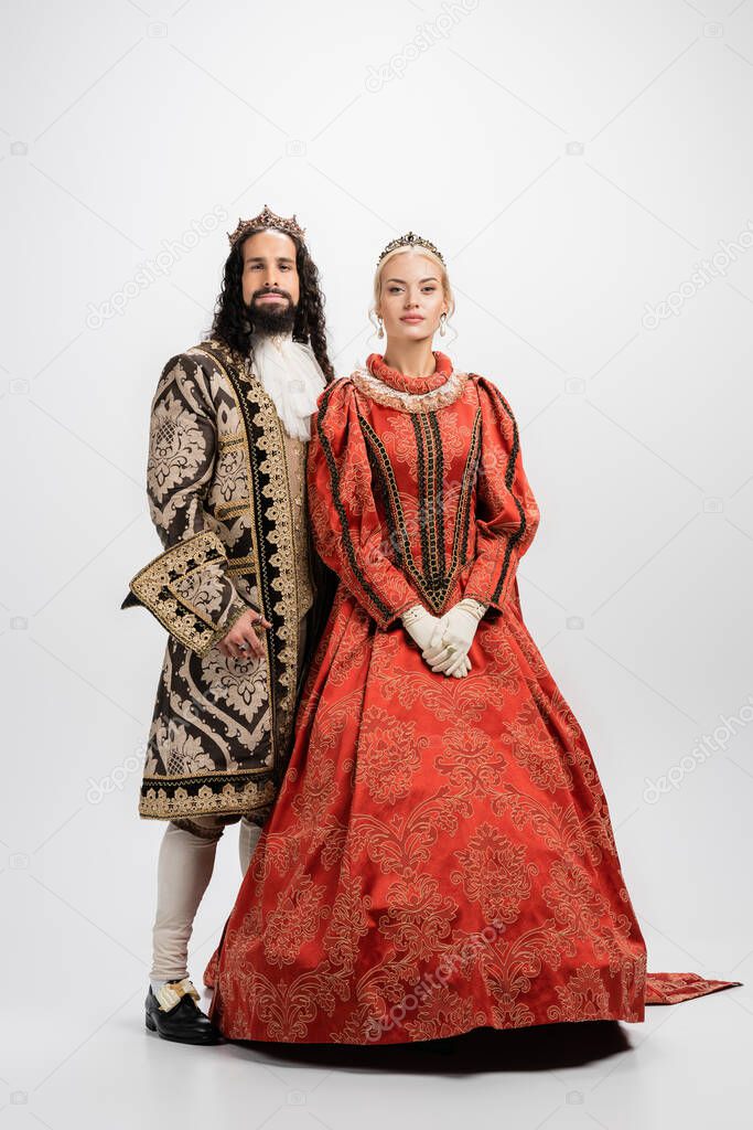 full length of historical interracial couple in golden crowns and medieval clothing on white