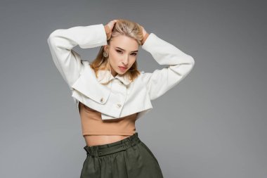 Kırlaşmış ceketli sarışın model, gri üzerinde yalnız poz veriyor.