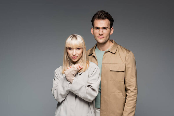 модные модели, позирующие при взгляде на камеру, изолированную на сером