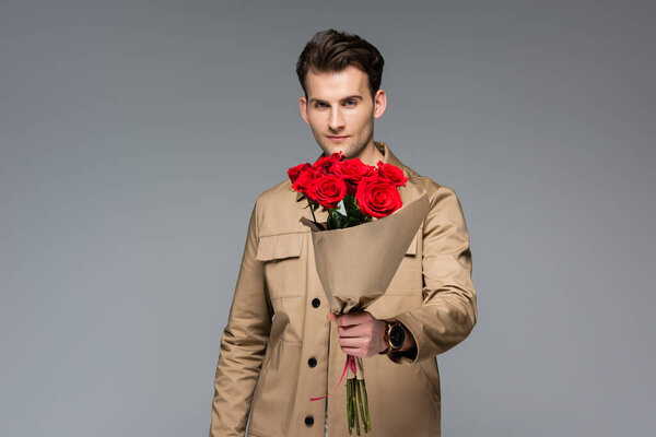 стильный мужчина держит букет из красных роз изолированы на серый