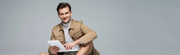 时尚男人笑着用灰色横幅隔离的数码平板电脑 — 图库照片