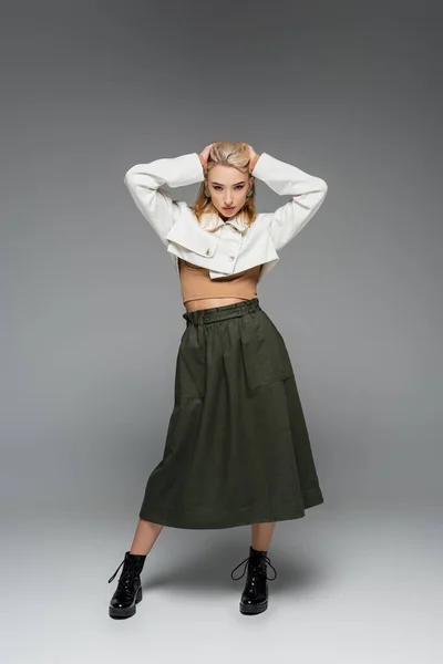 full length of blonde model in cropped jacket and skirt posing on grey