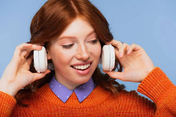 Feliz Ruiva Mulher Segurando Fones Ouvido Sem Fio Isolados Azul — Fotografia de Stock