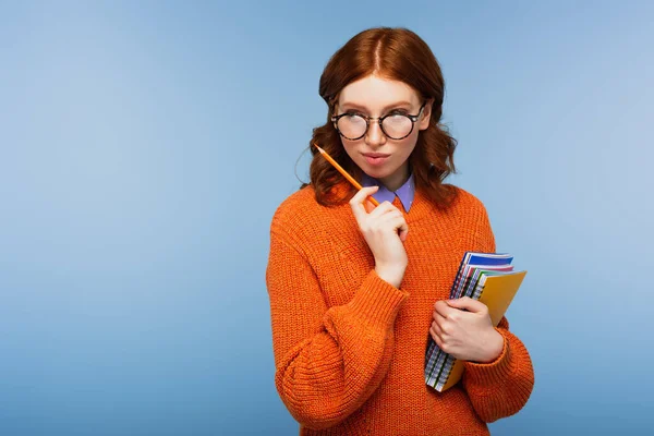 戴着眼镜 身穿橙色毛衣 头脑清醒的红头发学生 手里拿着笔记本和铅笔 蓝色隔离着 — 图库照片