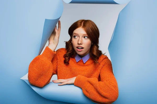 Überraschte Junge Frau Orangefarbenem Pullover Schaut Vor Blauem Zerrissenen Hintergrund — Stockfoto