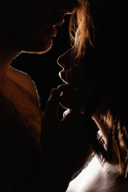 Siyah üzerine izole edilmiş seksi bir kadının dudaklarına dokunan adamı aydınlatmak.