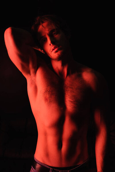 red lighting on sexy and muscular man standing isolated on black 
