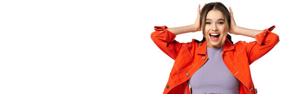 excited young woman in crop top and orange shirt with hands near head isolated on white, banner
