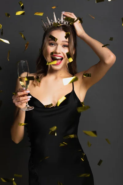 身穿黑色紧身衣头饰头饰 头戴香槟酒的快乐的年轻女子 在灰蒙蒙的五彩纸屑旁举着一杯香槟 — 图库照片